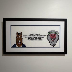 May include: Framed cross-stitch artwork featuring a cartoon horse and a bearded man. The text reads "IT GETS EASIER EVERY DAY IT GETS A LITTLE EASIER BUT YOU GOTTA DO IT EVERY DAY THAT'S THE HARD PART BUT IT DOES GET EASIER."