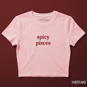 Peut inclure: Un haut court rose clair à manches courtes avec le texte "spicy pisces" en lettres rouge foncé sur la poitrine. L'étiquette intérieure du col affiche le texte "MERAKI" et le coin inférieur droit inclut la marque "MERAKI" en blanc.