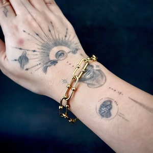 May include: A gold chain bracelet with a link design. The bracelet is on a person's wrist.