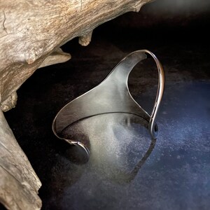 May include: A silver metal cuff bracelet with a unique, abstract design. The bracelet is open and has a smooth, polished finish.