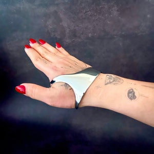 May include: A silver metal cuff bracelet with a unique, open design. The bracelet is worn on a person's wrist.