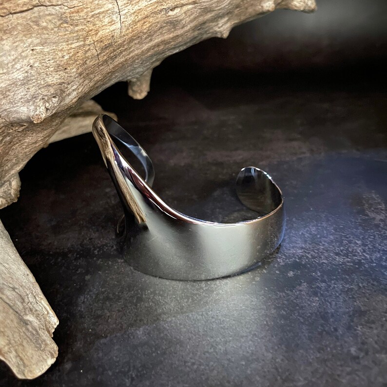 May include: A silver metal cuff bracelet with a curved, open design.