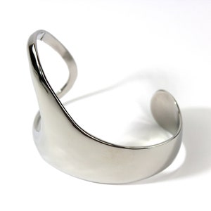 May include: A silver metal cuff bracelet with a unique, abstract design. The bracelet is open on one side and has a smooth, polished finish.