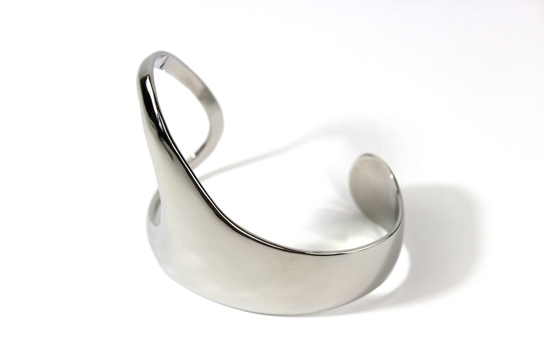 May include: A silver metal cuff bracelet with a unique, abstract design. The bracelet is open on one side and has a smooth, polished finish.