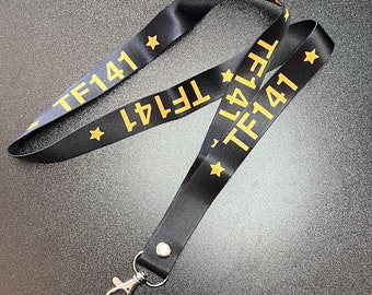 May include: Black lanyard with a gold clip and the text "TF141" repeated on both sides. The text is in a bold, sans-serif font.
