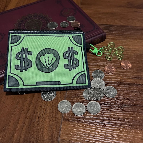 May include: A rectangular coin purse featuring a light green design that mimics a banknote with black dollar signs and a central shell icon. The purse has a black border, a black zipper, and a bright green flower-shaped zipper pull charm.