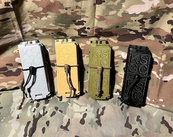 May include: Four different colored magazine pouches with the text "KSC SHIELD" embossed on the front. The pouches are made of a hard plastic and have a black elastic strap with a buckle.