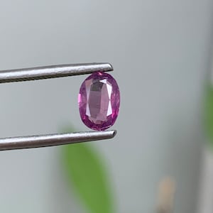 May include: A close-up of a pink oval gemstone held by tweezers.