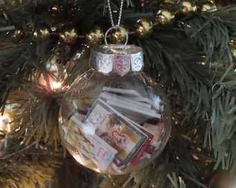 May include: A clear glass Christmas ornament with a silver top and a snowflake design. The ornament is filled with small, colorful books.