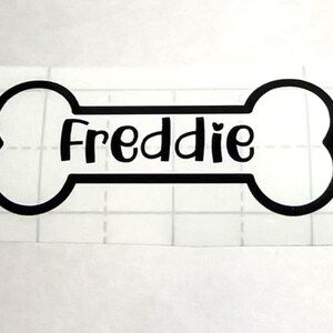 May include: Black vinyl sticker of a bone with the name Freddie written in a cursive font.