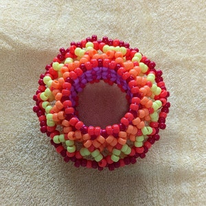 May include: A multi-coloured beaded bracelet with a circular design. The bracelet is made with red, orange, yellow, and pink beads.