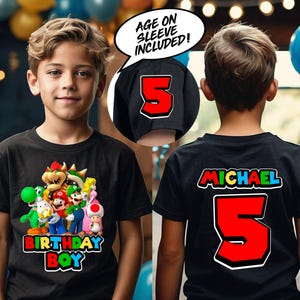 May include: Black t-shirt with a colorful graphic of Mario and friends from the Super Mario Bros. video game. The text "Birthday Boy" is printed below the graphic. The back of the shirt has a red number 5 and the name "Michael" printed in rainbow colors. The shirt has a black sleeve with a white number 5 printed on it. The text "Age on Sleeve Included!" is printed in a speech bubble.