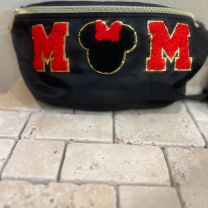 May include: Black fanny pack with a gold zipper and red felt letters that spell "MOM". A black felt Mickey Mouse head with a red bow is centered between the letters.