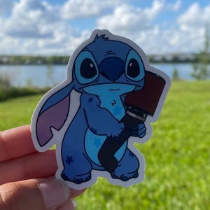 Puede incluir: Una pegatina azul del personaje Stitch con una cara grande y amigable y un filtro de aire rojo y negro en su mano.