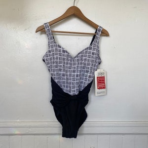 May include: A black and white geometric patterned swimsuit with a black bow detail at the waist. The swimsuit has a scoop neck and adjustable straps. The tag reads "Redefine".