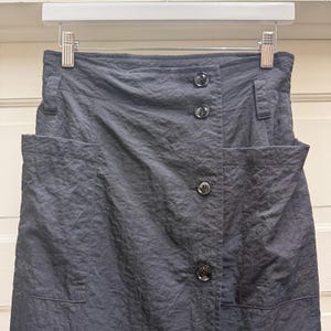 May include: A dark gray skirt with a button-up front and two large pockets. The skirt is hanging on a white hanger. The fabric has a textured, slightly wrinkled appearance.