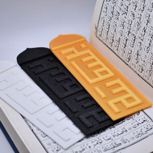 Puede incluir: Tres marcadores de diferentes colores con la palabra árabe "Allah" en relieve. Los marcadores están colocados encima de un libro abierto con texto árabe.