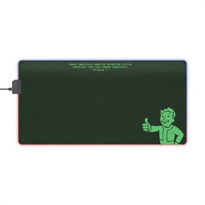 Peut inclure: Un tapis de souris vert et noir avec une bordure verte et une image pixelisée verte d'un homme levant le pouce. Le texte "ROBO-INDUSTRIES UNIFIED OPERATING SYSTEM COPYRIGHT 2075-2077 ROBO-INDUSTRIES -Display 1- " est affiché en vert sur le tapis de souris.