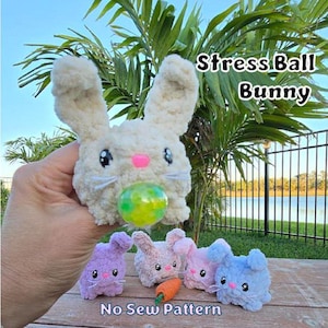 May include: Four plush bunny stress balls in different colors: purple, pink, light pink, and blue. The bunnies have embroidered eyes and noses. The larger bunny in the center is holding a green and yellow stress ball. The text "Stress Ball Bunny" and "No Sew Pattern" are visible in the image.