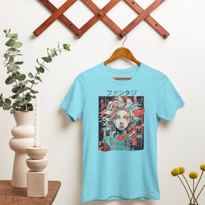 May include: A light blue t-shirt with a graphic print of a woman's face in a colorful, geometric style. The text "ファンタジー" is printed above the graphic.