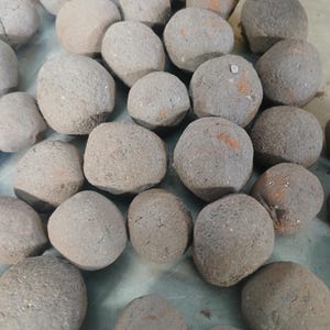 May include: A close-up of a group of dark gray, round, textured stones. The stones are arranged in a random pattern on a light gray surface.