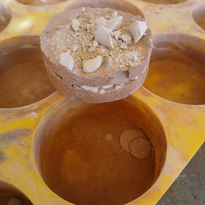 May include: A yellow silicone mold with eight round cavities. One cavity is filled with a brown mixture topped with small white pieces.