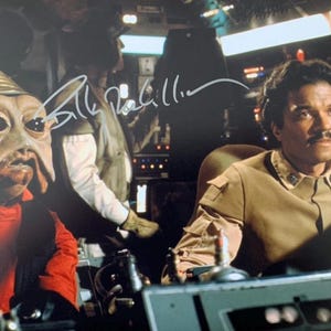 May include: A signed photograph of a scene from the Star Wars film featuring a character with green skin and large eyes, and a character with dark hair and a moustache. The signature reads "Bill Pullman".