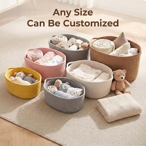 May include: A collection of oval-shaped woven rope storage baskets in yellow, pink, gray, white, and brown, containing various folded blankets and plush toys. The text "Any Size Can Be Customized" is displayed in brown letters above the baskets.