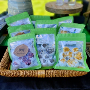 May include: A wicker basket filled with clear plastic bags containing handmade shower steamers. The bags are labeled with the text "Sweet Edition" and the scents "Lush Lavender" and "Peppermint Pine".
