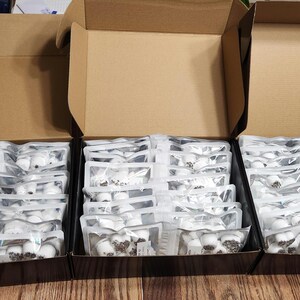 May include: Three cardboard boxes filled with individually packaged white items. The boxes are open and the items are visible.