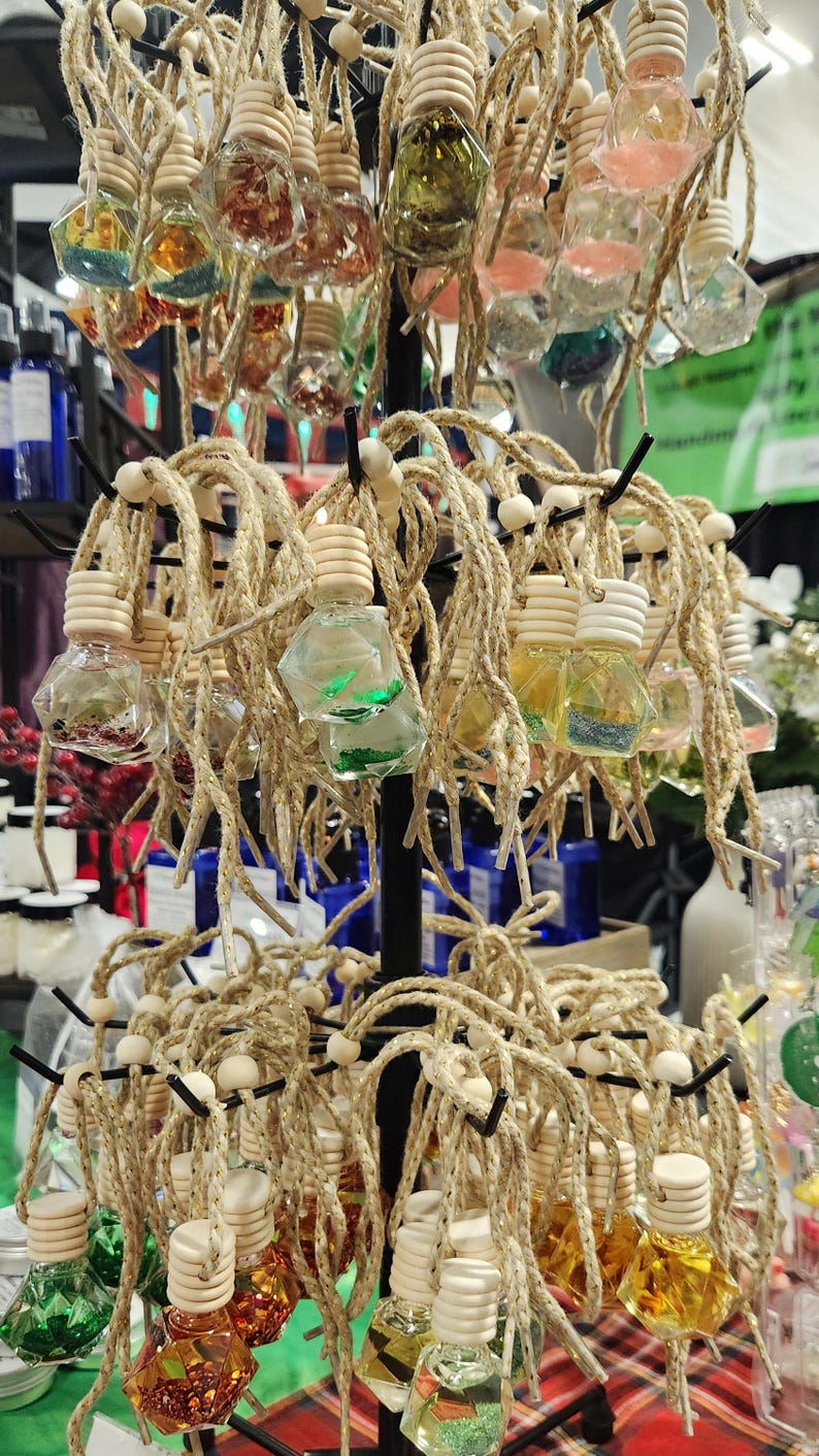 May include: A display of small, clear glass bottles with cork tops and twine hangers. The bottles are filled with colorful glitter and are arranged in a tiered display.