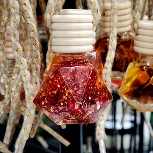 May include: A close-up of a red and gold glitter car air freshener hanging from a string. The air freshener is shaped like a diamond and has a wooden top.