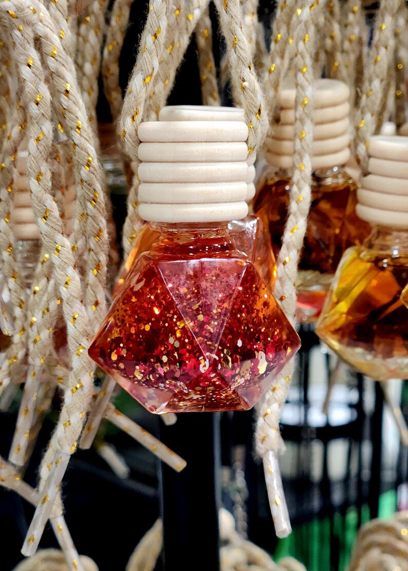 May include: A close-up of a red and gold glitter car air freshener hanging from a string. The air freshener is shaped like a diamond and has a wooden top.