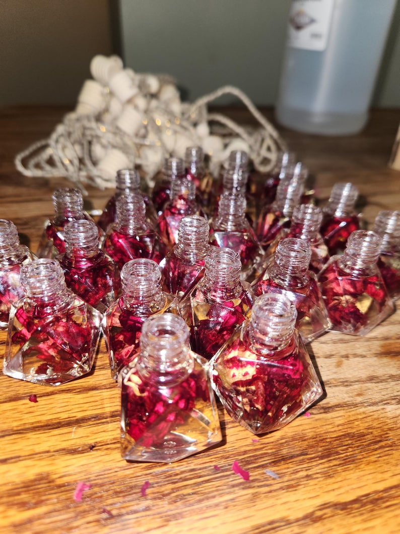May include: A collection of small, clear glass bottles filled with dried red rose petals and a clear liquid. The bottles are shaped like diamonds and have a cork stopper.