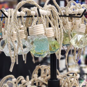 May include: A display of decorative car air fresheners with a variety of colors and designs. The air fresheners are made of glass and have a geometric shape. They are hanging from a metal rack with twine and wooden beads.