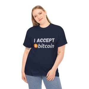 May include: A navy blue t-shirt with the text "I ACCEPT Bitcoin" in white. The Bitcoin logo is orange and white. The shirt is a casual style.