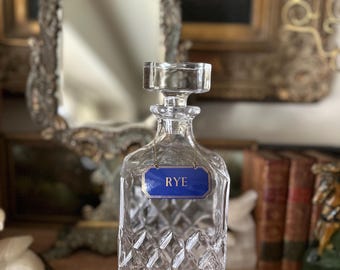 Può includere: Una caraffa di vetro trasparente con un motivo a diamante e un'etichetta blu che dice "RYE".