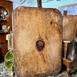 May include: A large, rectangular wooden cutting board with a natural wood finish. The board has a large knot in the center and shows signs of wear and use. The board has a handle on the top.