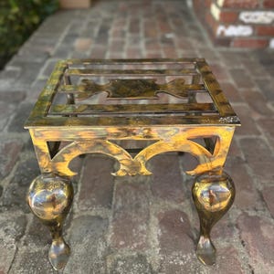 May include: A square, ornate metal side table with a gold and bronze finish. The table has a decorative openwork top and four bulbous legs. The table is approximately 18 inches square and 18 inches tall.