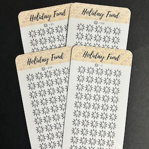 May include: Four white cards with a glittery floral border and the words "Holiday Fund" printed at the top. Each card has a different value: £5, £10, £20, and £. Each card features a grid of smiling sun illustrations.