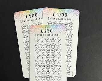 May include: Three white saving challenge cards with rainbow-colored accents. The cards have text indicating saving goals of £250, £500, and £1000. Each card features star-shaped boxes for tracking savings, with amounts like £5, £10, and £20.