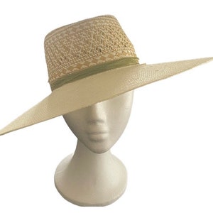 Puede incluir: Un sombrero de paja de ala ancha con un patrón tejido y una cinta verde alrededor de la corona. El sombrero es blanco y tiene una ala ancha que proporciona sombra del sol.