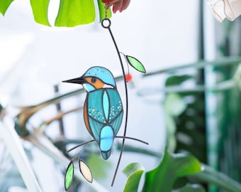 May include: A stained glass bird ornament depicting a kingfisher perched on a branch with a red berry. The bird is blue, green, and brown with a detailed design.