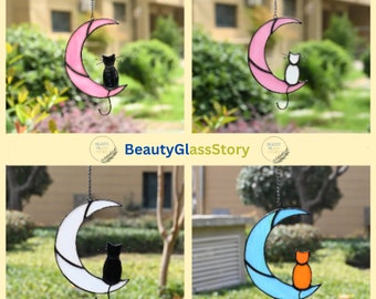 May include: Four stained glass cat and crescent moon suncatchers. The suncatchers are hanging from a chain. The cats are black, white, and orange. The moons are pink, white, and blue.