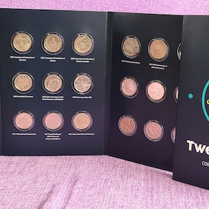 May include: A black coin collection folder with a yellow and blue logo of a platypus. The folder has the text "Royal Australian Mint" and "Twenty Cent Coin Collection Folder".
