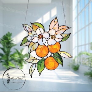 Puede incluir: Una ventana de vitral colgada de una cadena. El diseño presenta flores blancas con centros amarillos y fruta naranja. El fondo es azul claro.