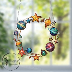 May include: A stained glass suncatcher with a circular design featuring planets and stars. The planets are painted in vibrant colors, including blue, green, red, and yellow. The stars are gold and yellow. The suncatcher is hanging from a silver chain.