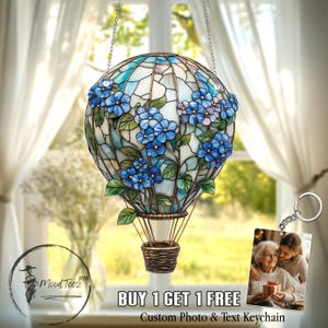May include: A stained glass hot air balloon keychain with blue flowers and green leaves. The balloon is hanging from a silver chain. The keychain also includes a separate photo frame keychain with a picture of two women. The text "BUY 1 GET 1 FREE Custom Photo & Text Keychain" is displayed below the image.