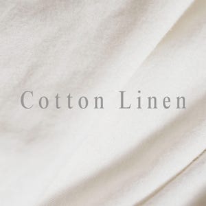 May include: Close-up of off-white cotton linen fabric with soft folds. The text "Cotton Linen" is printed in a light gray color across the fabric. The fabric appears to be smooth and slightly textured.