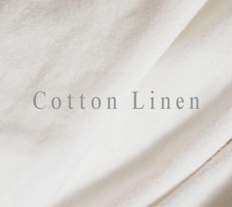 May include: Close-up of off-white cotton linen fabric with soft folds. The text "Cotton Linen" is printed in a light gray color across the fabric. The fabric appears to be smooth and slightly textured.